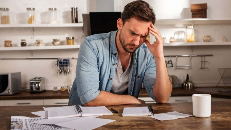 Distressed looking man at kitchen island with financial paperwork