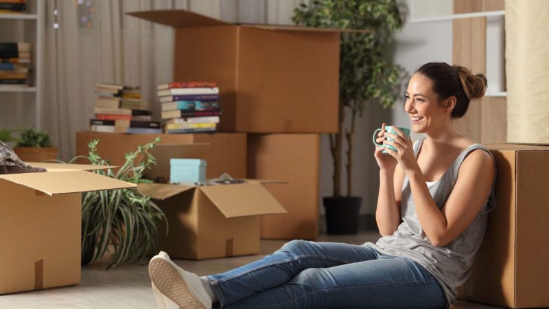 Smiling young woman sitting on floor surrounded by moving boxes